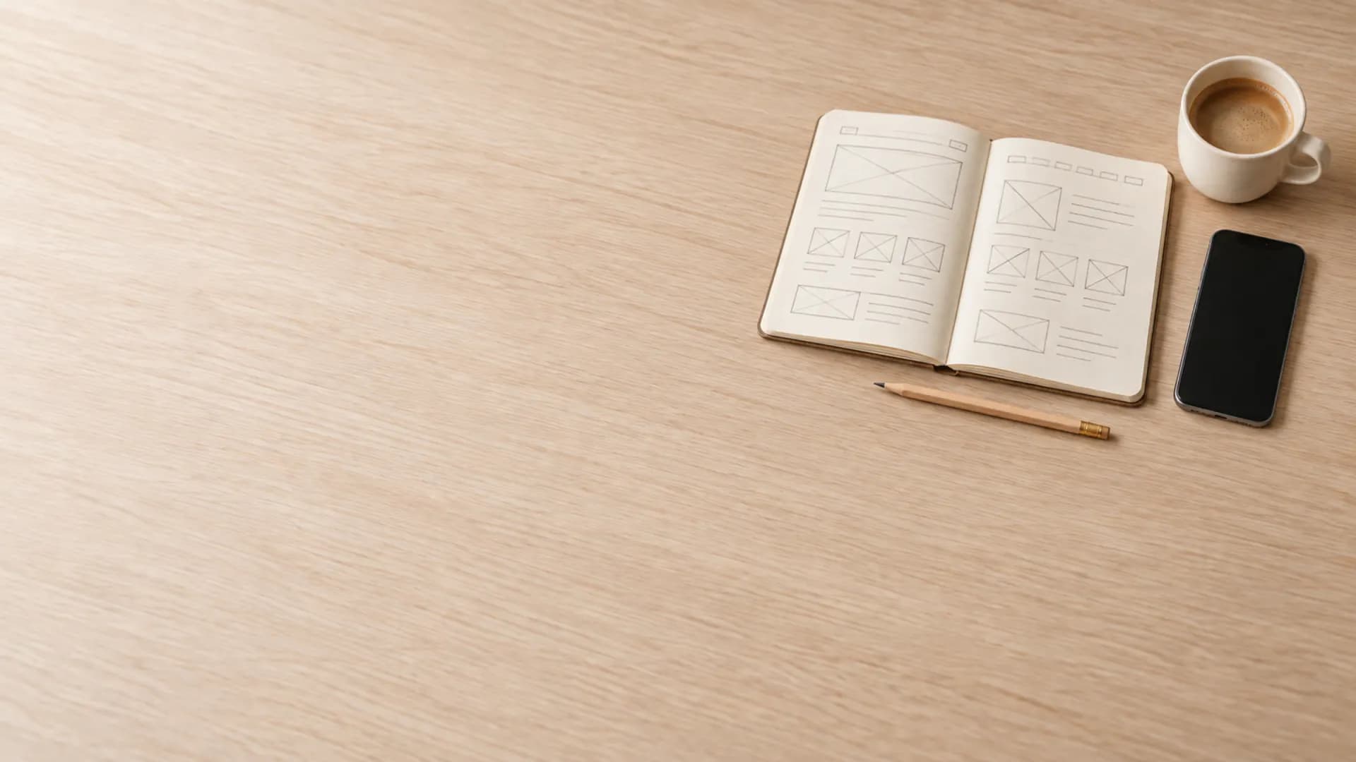 Aufgeschlagenes Notizbuch mit einer von Hand skizzierten Website, daneben Bleistift, Kaffee und Smartphone